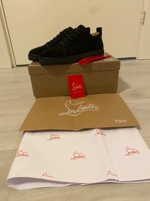 Svarta sneakers från Christian Louboutin - Stilrena svarta sneakers från Christian Louboutin i mocka med klassisk röd sula och svarta skosnören. Låg modell med rund tå och diskret logga på sulan. Kommer med originalkartong, skopåse och skohorn. Helt nya. Pris går att diskutera.