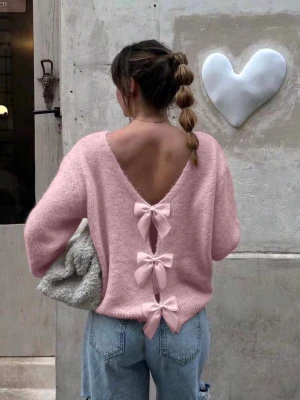 Rosa stickad tröja med rosetter - OBS!! Ingen lapp i nacken finns då tröjan har öppen rygg, lapp i midjan är kvar. Supersöt ljusrosa stickad tröja med djup v-ringning i ryggen och tre stora matchande rosetter längs ryggen. Tröjan har lång ärm, avslappnad passform och ribbade muddar. Perfekt för dig som vill ha en gullig och trendig look.