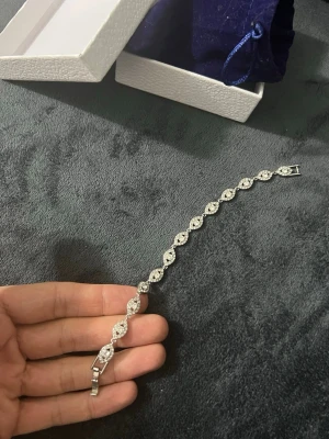 Silverfärgat armband med gnistrande stenar - Snyggt armband i silverfärg med glittrande stenar i ett elegant, vågformat mönster. Armbandet har små, infattade stenar som ger en exklusiv känsla och stängs med ett smidigt spänne. Perfekt accessoar för dig som gillar stilrena smycken med lite extra bling.