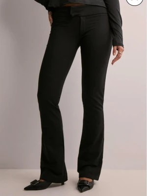 Soft flare Nelly kostymbyxor - Säljer ett par svarta kostymbyxor med utsvängda ben och låg midja. Byxorna har en stilren look med diskreta fickor och klassisk stängning fram. Materialet känns mjukt och stretchigt vilket gör dem riktigt bekväma att bära.