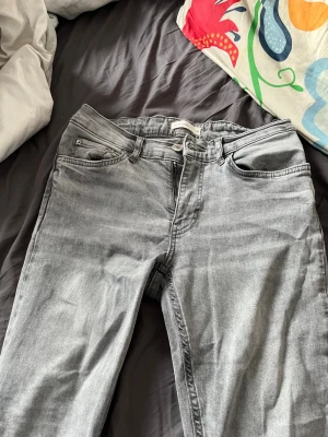 Grå raka jeans från Gina - Säljer ett par grå jeans från Gina med rak passform och klassisk femficksdesign. Jeansen har bälteshällor, knappgylf och är tillverkade i ett mjukt denimtyg. Perfekta för en avslappnad och trendig look.