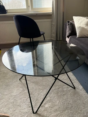 Runt soffbord med glasskiva - Säljer ett stilrent runt soffbord med transparent glasskiva och svarta metallben i modern design. Bordet har en enkel men trendig look som passar perfekt till vardagsrummet. Metallbenen är formade i ett geometriskt mönster för extra detalj. Finns att hämta i Göteborg