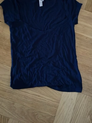 Mörkblå v-ringad topp med spets detaljer  - En enkel mörkblå topp med v-ringning, spets detaljer och korta ärmar. Toppen har en mjuk och lätt känsla, perfekt för en avslappnad stil. 