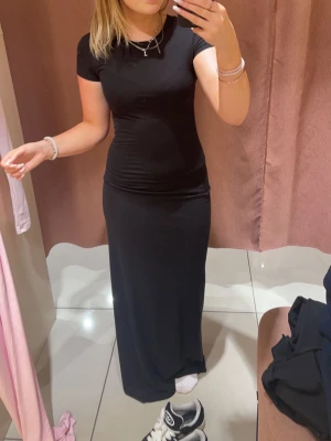 Svart långklänning med kort ärm - En stilren svart långklänning med rund halsringning och korta ärmar. Klänningen har en figurnära passform och är tillverkad i ett mjukt och stretchigt material som ger en bekväm känsla. Perfekt för dig som gillar en enkel och klassisk look.