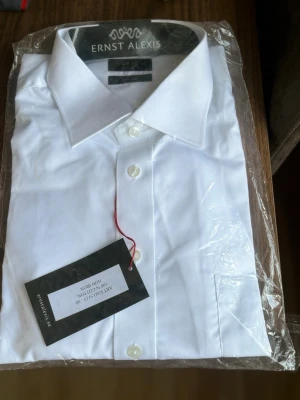 Vit skjorta från Ernst Alexis - Klassisk vit skjorta från Ernst Alexis i 100% bomull. Skjortan har knappar framtill, normal passform och en stilren krage. Perfekt för en clean och tidlös look.