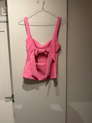 Rosa trendig Zara topp - Supersnygg rosa trendig Zara topp med breda axelband och en stor rosett baktill. Toppen har en figurnära passform och är perfekt för att sticka ut. Materialet känns som polyester och toppen har en modern, trendig look.