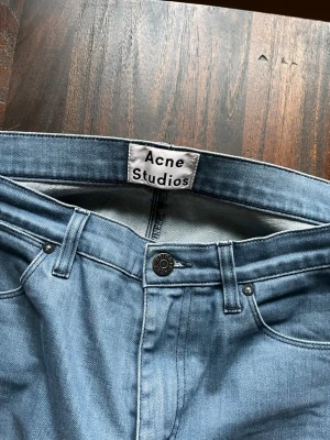 Ljusblå jeans från Acne Studios - Säljer ett par ljusblå jeans från Acne Studios med klassisk femficksdesign och raka ben. Jeansen har en snygg knappstängning och är tillverkade i denim. Perfekt för dig som gillar stilrena och trendiga jeans.