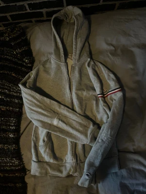Grå zip hoodie från Moncler - En grå hoodie ifrån Moncler som aldrig används längre, köpte den av en kompis 2024, flera tecken på skador samt lagningar, storleken säger M men passar mer S-Xs, Pris är diskuterbart 