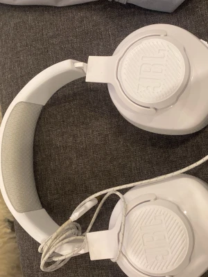 Vita over-ear hörlurar från JBL - Snygga vita over-ear hörlurar från JBL med vadderad bygel och mjuka öronkuddar i grått. Hörlurarna har sladd med 3,5 mm kontakt och tydliga L/R-markeringar på insidan. Perfekta för musik, gaming eller filmkvällar.