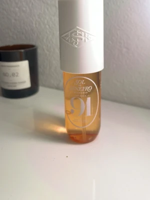 Sol de Janeiro 91 Parfym - Sol de Janeiro 91 är en parfym i en stilren, genomskinlig flaska med vit kork. Flaskan har en varm orange ton och modern design. Doften beskrivs med noter av rosa ros, passionsfrukt och karamell. Perfekt för dig som gillar fräscha och söta dofter.