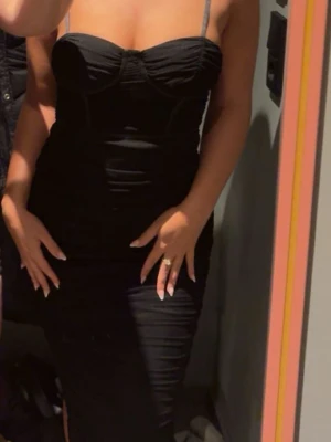 Svart figurnära långklänning - Säljer en svart långklänning med smala axelband och markerad byst. Klänningen har en tight passform och en stilren, enkel design som framhäver figuren. Perfekt för dig som vill ha en klassisk och elegant look.