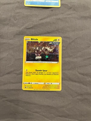 Pokémonkort Blitzle Rapid Strike - Säljer ett Pokémonkort med Blitzle från Rapid Strike-serien. Kortet är färgglatt med gul ram och motiv av Blitzle i en nattmiljö. Materialet är klassiskt laminerat papper och kortet har Thunder Spear-attack. Perfekt för samlare och Pokémon-fans!