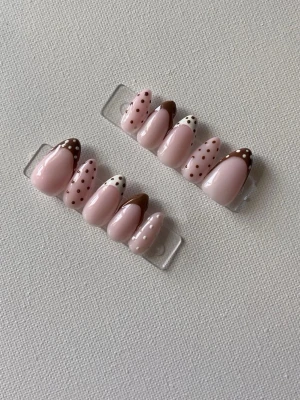 Bruna och rosa prickiga press-on naglar - Snygga press-on naglar i mandelform med ljusrosa bas och bruna samt vita prickiga detaljer. Några naglar har bruna tippar med vita prickar, andra har rosa tippar med bruna prickar. Perfekt för dig som vill ha en lekfull och trendig nagelstil.