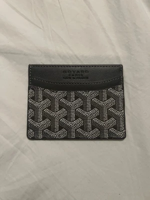 Grå plånbok/korthållare - Snyggt grått kortfodral med det klassiska vita och gråa mönstret. Tillverkat i läder och canvas med präglad logotyp på framsidan. Perfekt för kort och sedlar, smidig att ha i fickan. Postar senast dagen efter du köpt. Skriv om du har några frågor