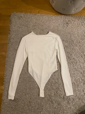 Vit långärmad body - Säljer en stilren vit body med långa ärmar och rund halsringning. Bodyn har klassisk passform och knäppning i grenen. Perfekt att styla med jeans eller kjol för en clean look.
