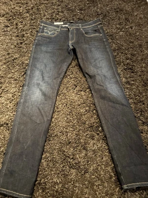Mörkblå slim jeans från Replay 34/32 - Snygga mörkblå slim fit jeans från Replay med klassiska fem fickor och kontrastsömmar. Jeansen har en stilren look och är tillverkade i denim med en lätt stretch för extra komfort. Perfekta för dig som gillar en modern och smal siluett.