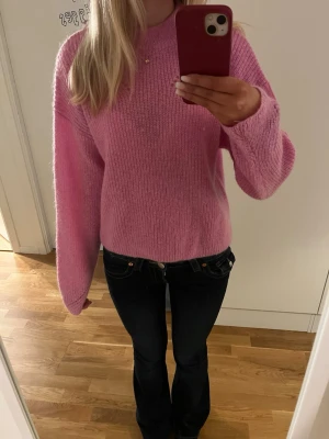 Rosa stickad tröja - Mysig rosa stickad tröja med rund hals. Tröjan har en lös passform och ett diskret hålmönster vid axeln. Perfekt för dig som gillar en färgglad och trendig look.