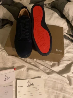 Mörkblå sneakers från Christian Louboutin - Snygga mörkblå sneakers från Christian Louboutin i mocka med klassisk röd sula och broderad logga bak. Skorna har rund tå, snörning och platt sula. Perfekta för dig som vill sticka ut med exklusiva detaljer och ikonisk design. Använda i två veckor innan jag tröttnade på att dem var lite för stora. Kom gärna med bud! Bilderna är från när dem var nya så dem är inte helt identiska i användningen som på bild 