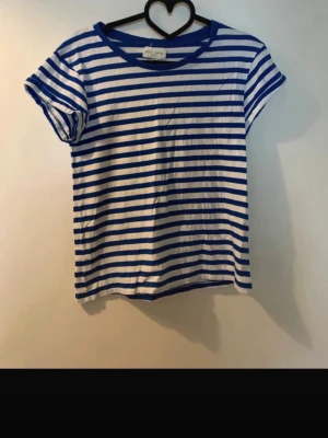 Randig blåvit t-shirt från Monki - Säljer en klassisk t-shirt från Monki med blå och vita ränder. T-shirten har korta ärmar och en rund halsringning. Materialet är mjuk bomull och passformen är normal. Perfekt för dig som gillar en enkel och stilren look.