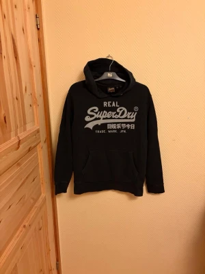Real Superdry Hoodie  - En snygg Superdry Hoodie! Skick 8/10 🤩                   Defekter inga snören samt att tyget har släppt lite vid halsen. Storlek L 🙌                                                     Skriv vid mera frågor/bilder 💬