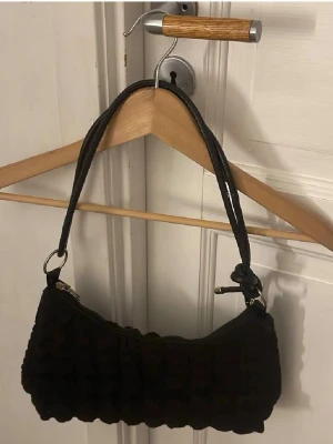 Svart quiltad handväska - Trendig svart handväska med quiltad design och kort axelrem. Perfekt storlek för det viktigaste och enkel att matcha med olika outfits. Väskan har dragkedja upptill och stilren look.