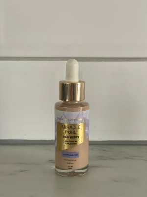 Max Factor Miracle Pure Foundation - Max Factor Miracle Pure Skin Reset Foundation i glasflaska med pipett och guldfärgat lock. Färgen är ljus beige (18-30 Fair) och formulan är en 2-i-1 serum foundation som jämnar ut hudtonen. Innehåller 2% niacinamid och är framtagen för en naturlig finish.
