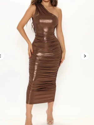 Brun metallic one shoulder klänning - Snygg brun metallic klänning med one shoulder-design och figurnära passform. Klänningen har rynkade detaljer längs sidorna och är i en glansig syntetmix som ger en lyxig känsla. Perfekt för dig som vill sticka ut med en trendig look. Från fashionova 
