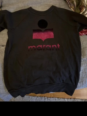 Svart sweatshirt från Isabel Marant - Cool svart sweatshirt från Isabel Marant Étoile med rosa sammetstryck och logga framtill. Tröjan har rund halsringning och är tillverkad i mjukt bomullsmaterial. Perfekt för en avslappnad och trendig look.