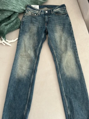 Blå raka jeans med slitningar - Säljer ett par blå jeans med raka ben och snygga slitningar framtill. Jeansen har klassisk femficksdesign och normalhög midja. Perfekta för en avslappnad och trendig look.