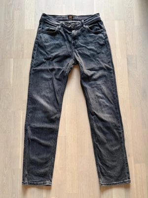 Mörkgrå raka jeans från Lee - Säljer ett par mörkgrå jeans från Lee med rak passform och klassisk femficksdesign. Jeansen är tillverkade i ett robust denimtyg. Storlek: W31 L32