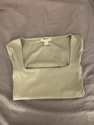 Ljusgrå topp med fyrkantig ringning - Trendig ljusgrön topp från Amisu med korta ärmar och snygg fyrkantig ringning. Tillverkad i mjukt och stretchigt material som sitter skönt på kroppen. Perfekt att styla med jeans eller kjol för en clean look🤗❤️