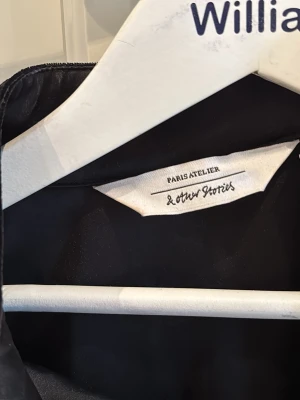 Svart sammetskappa/klänning & Other Stories - Elegant svart sammetskappa/klänning från & Other Stories Paris Atelier med glittrande blomformade knappar. Klassisk krage och lyxig känsla, perfekt för dig som vill sticka ut med en unik detalj. Snygg och tidlös design. Inte en kappa riktigt utan mer än klänning 