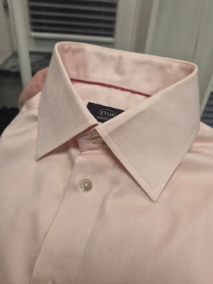 Eton "Ganghester 1928" ljusrosa skjorta, storlek 15½ 39 - Stilren ljusrosa skjorta från Eton med klassisk krage och bröstficka. Skjortan har knappar framtill och långa ärmar. Perfekt för dig som vill ha en clean och snygg look.