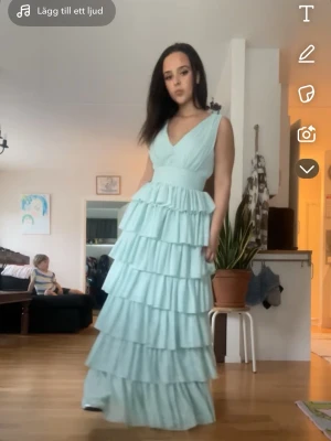 Ljusgrön Balklänning med volanger - Superfin balklänning i ljusgrönt med flera lager volanger och v-ringad hals och rygg. Klänningen har breda axelband och markerad midja som ger en elegant siluett. Perfekt för skolbal bröllop eller annat. Kan gå ner i pris vid snabb affär.