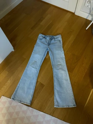 Ljusblå bootcut jeans - Säljer ett par ljusblå bootcut jeans med klassisk femficksmodell och låg midja. Jeansen har en snygg tvättad look och är tillverkade i ett mjukt denimtyg som sitter skönt. Perfekta för dig som gillar retrovibbar och vill ha ett par jeans med lite vidare ben.