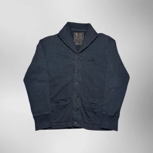 Vintage Ralph Lauren button up kofta - herr strl M - Säljer en vintage Ralph Lauren button up kofta i mörkgrå färg i storlek M med vintage broderad Ralph Lauren logga på vänster sida av bröstkorgen. Stickad krage och två fickor vid midjan.  👕 Märke: Ralph Lauren 📏 Storlek: M 🎨 Färg: Mörkgrå 🧵 Material: 88% bomull, 12% akryl 📐 Mått: 70 cm lång, 55 cm bred 📌 Skick: Mycket bra skick (se bilder)  💬 Hör av dig vid frågor 💰 Pris kan diskuteras vid snabb affär 📦 Skickas inom 24 timmar