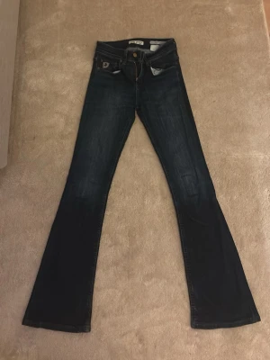 Mörkblå bootcut Jeans från Lois  - Snygga mörkblå märkes jeans. Är bootcut jeans från Lois med klassisk femficksdesign och gulddetaljer på knappar och nitar. Jeansen har en diskret tvättad look och är tillverkade i stretchigt denim för en bekväm passform. Perfekta till vardags! Modell melrose, köptes för 1800kr på nk.
