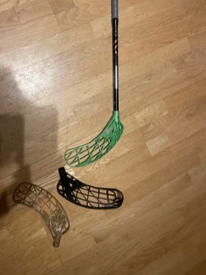 Innebandyklubba oxdog med grönt opti light blad, längd 96 flex 29, kommer med två blad, avox svart och optilight brun, bra skick på bladen förutom det gröna som har en liten spricka, klubban är i bra kvalitet med bra skick - Säljer en Oxdog innebandyklubba med svart och kopparfärgat skaft samt grönt blad. Två extra blad i svart och beige ingår. Bladen är av plast och har ett öppet rutmönster för bättre bollkontroll. Perfekt för dig som vill ha flera alternativ på planen.