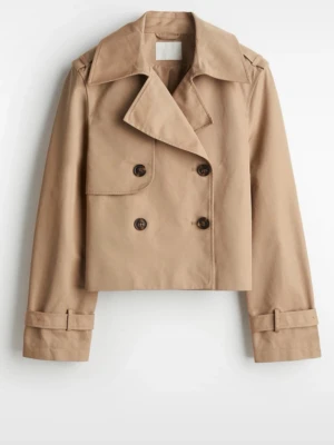 Kort beige trenchcoat  - Trendig kort trenchcoat i beige med klassisk dubbelknäppning och bred krage. Jackan har snygga detaljer som axelklaffar och justerbara spännen vid ärmsluten. Perfekt för dig som vill ha en stilren och modern look. Materialet är slätt och känns tåligt.