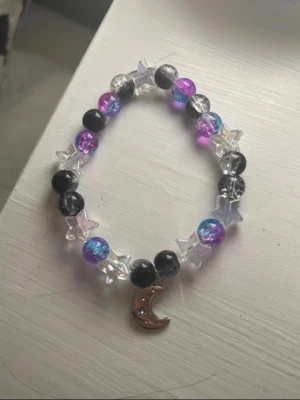 Stjärn- och månarmband med pärlor - Unikt handjort armband av mig  med pärlor i svart, lila, blått och genomskinligt, blandat med stjärnformade pärlor och en månhänge i metall. 18cm omkrets❤️