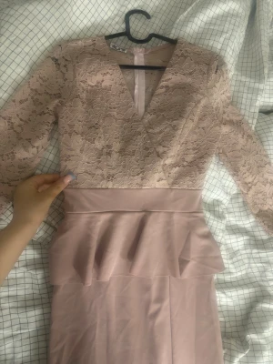 Ljusrosa spetsklänning med volang - Söt ljusrosa klänning med v-ringad spetsöverdel och trekvartsärm. Kjolen har en snygg volangdetalj i midjan och är figurnära🩷