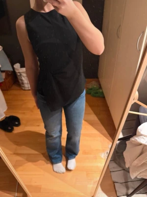 Svart ärmlös topp från Bik Bok - Snygg svart ärmlös topp från Bik Bok med hög halsringning och figurnära passform. Toppen har en stilren design utan mönster och är tillverkad i ett mjukt, stretchigt material som känns bekvämt mot huden. Perfekt att matcha med jeans eller kjol.