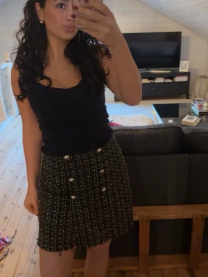 Svart och vit rutig kortkjol med knappar - Säljer en svart och vit rutig kortkjol med dekorativa knappar framtill. Jätte classy kjol!!