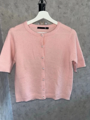 Ljusrosa kofta med pärlknappar - Supersöt ljusrosa kofta från Lager 157 med  korta ärmar och rund halsringning. Koftan har pärlknappar framtill. Nästan helt oanvänd🎀