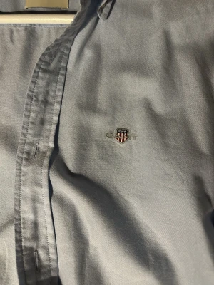 Ljusblå slimfit skjorta från GANT - Säljer en klassisk ljusblå oxfordskjorta från GANT i slim fit-modell. Skjortan har broderad logga på bröstet, knappar framtill och är tillverkad i mjuk bomull. Perfekt för en clean och stilren look.