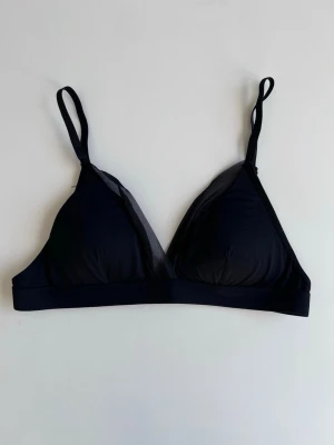 Svart vadderad triangel-bh med meshdetaljer (utan bygel) - Svart triangel-bh modell med tunna, justerbara axelband, meshdetaljer, vadderade kupor och ingen bygel. Perfekt för dig som är ute efter en enkel och skön bh. Passar lika bra under t-shirts som linnen. Knappt använd.
