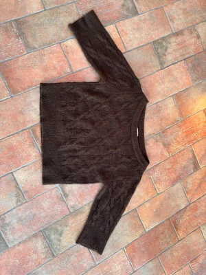 Mörkbrun kabelstickad tröja - Mysig mörkbrun stickad tröja med kabelstickat mönster och båthalsringning. Man kan ha den hängandes ner för valfri axel eller båda. Köpt på Gina young men passar som en storlek S! Skicket är jättefint och finns knappast tecken på användning!