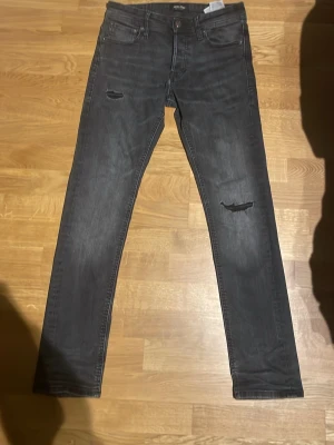 Svarta slim fit jeans med slitningar - Snygga svarta slim fit jeans med slitna detaljer på låren och knäna. Klassisk femficksmodell med dragkedja och knapp. Jeansen har en tvättad look och raka ben, perfekta för en cool och avslappnad stil.