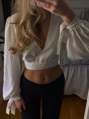 Vit omlottopp med knyt från NA-KD - Säljer en superfin vit omlottopp från NA-KD. Toppen har långa puffärmar med knyt vid handlederna, djup v-ringning och croppad passform. Använd ett fåtal gånger 