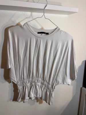 Vit  topp M - Vit croppad topp från lager 157 med rund halsringning och resår i midjan som ger en snygg rynkad effekt. 